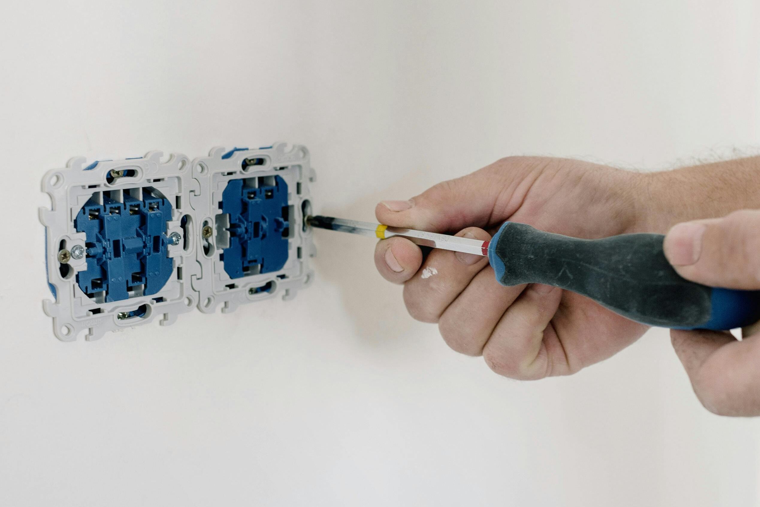 Close-up of hands using a screwdriver to install electrical sockets on a white wall.